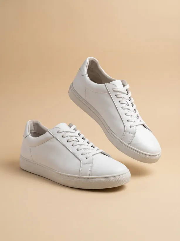 The same sneakers on a seamless sand background in studio light, one floating above the other