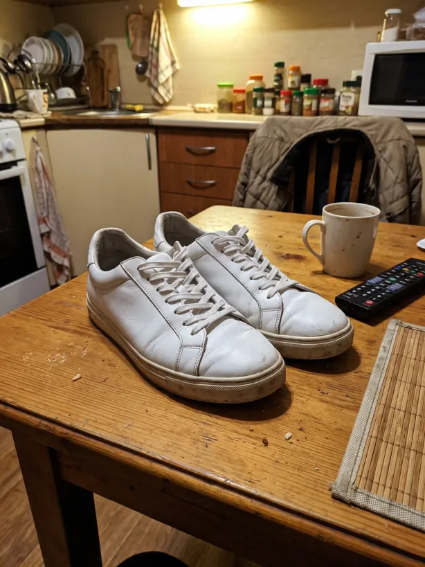 White leather sneakers on a kitchen table under yellow light, a phone snapshot